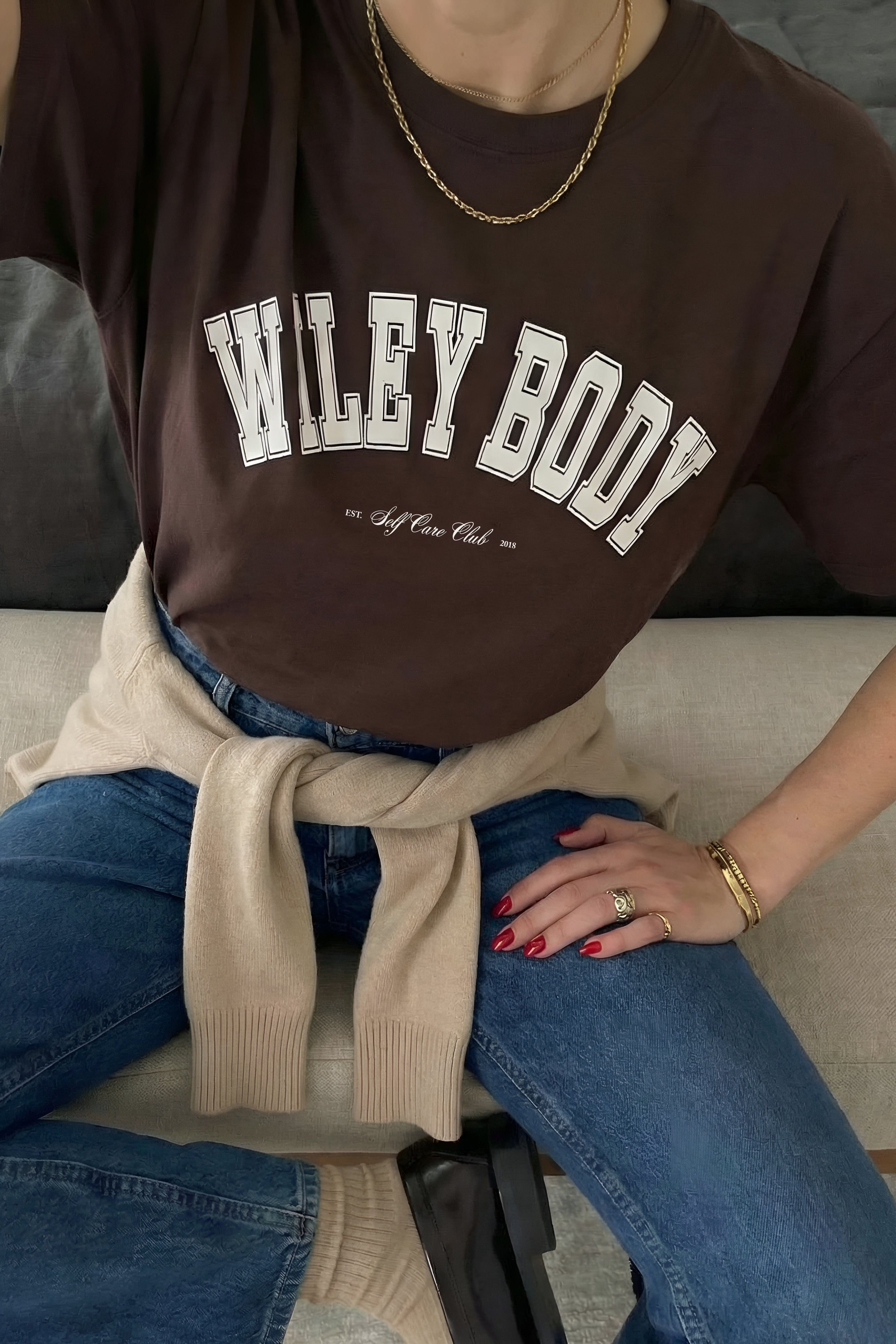 Person wearing a brown 'WILEY BODY' t-shirt sitting on a couch.