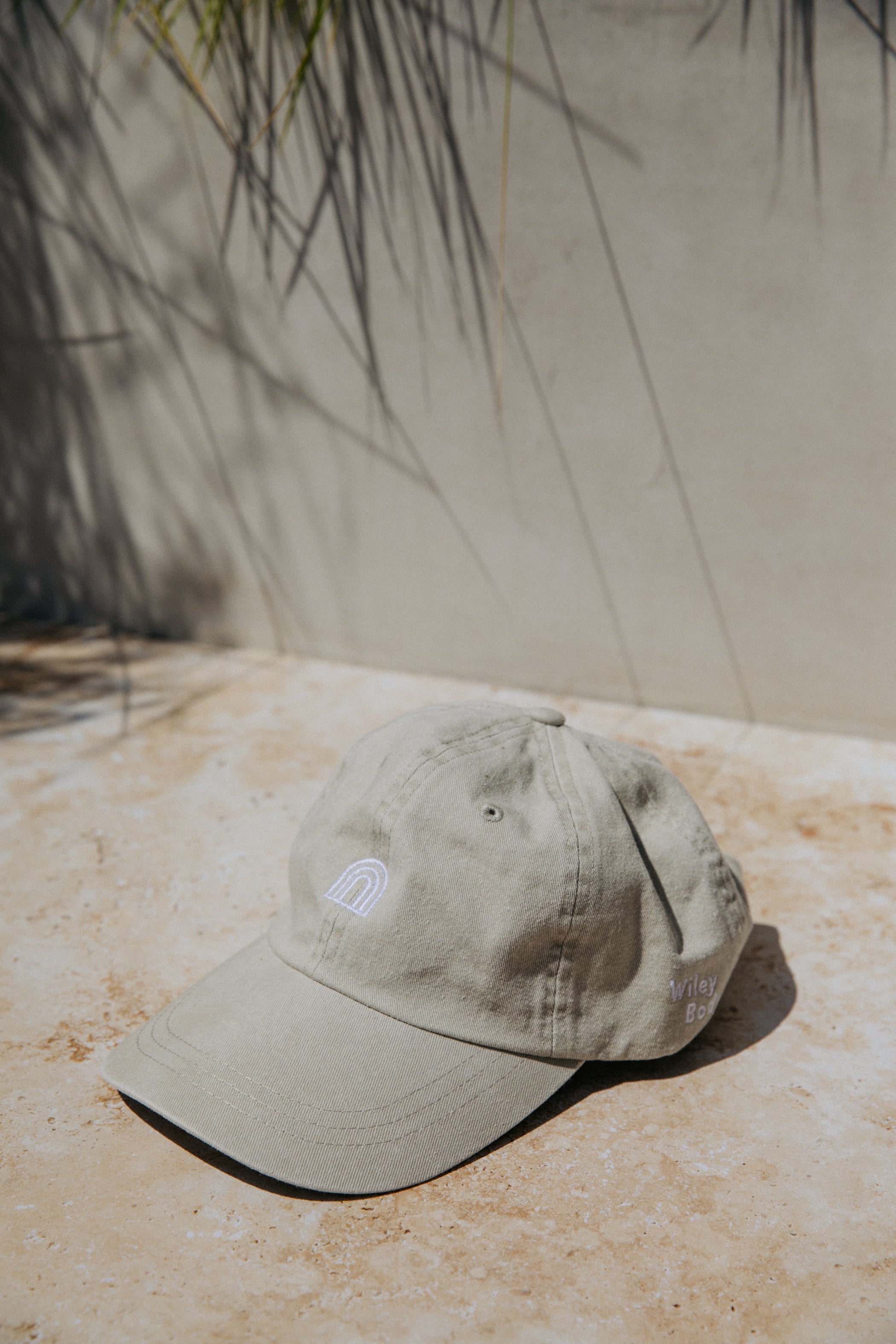 The fog color wiley baseball hat with the rainbow logo embroidered on the front center of the hat and the Wiley Body logo on the left side of the hat