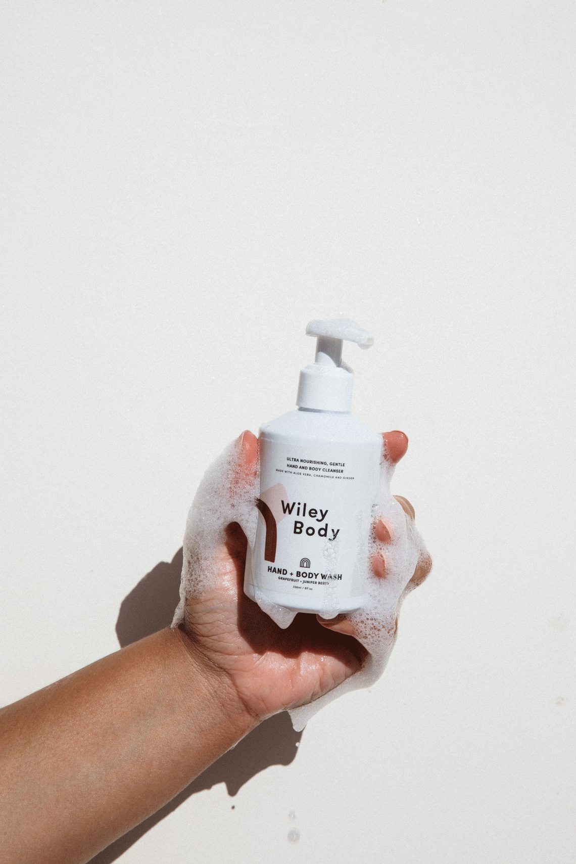 A GIF showing a brown arm holding a white bottle that says hand & body wash with bubble running down the bottle