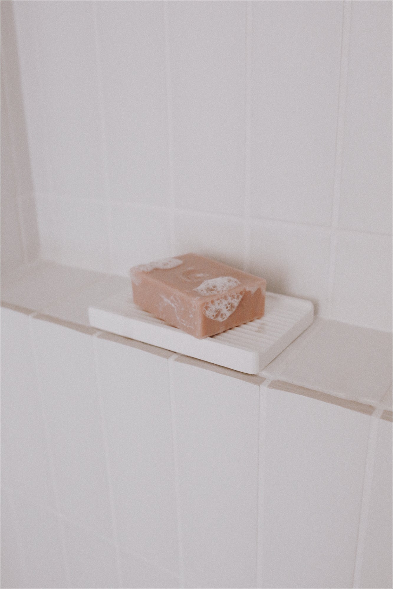 A photo of a Body Bar and Soap Dish on a shelf in a shower with bubbles on the Body Bar