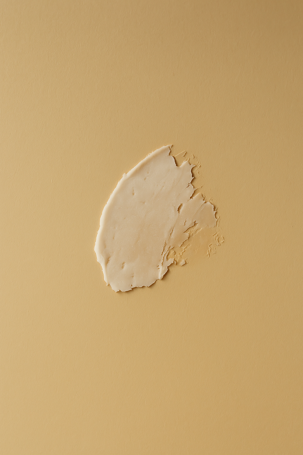 A close-up of a creamy, off-white lip balm formula smeared on a smooth beige background.