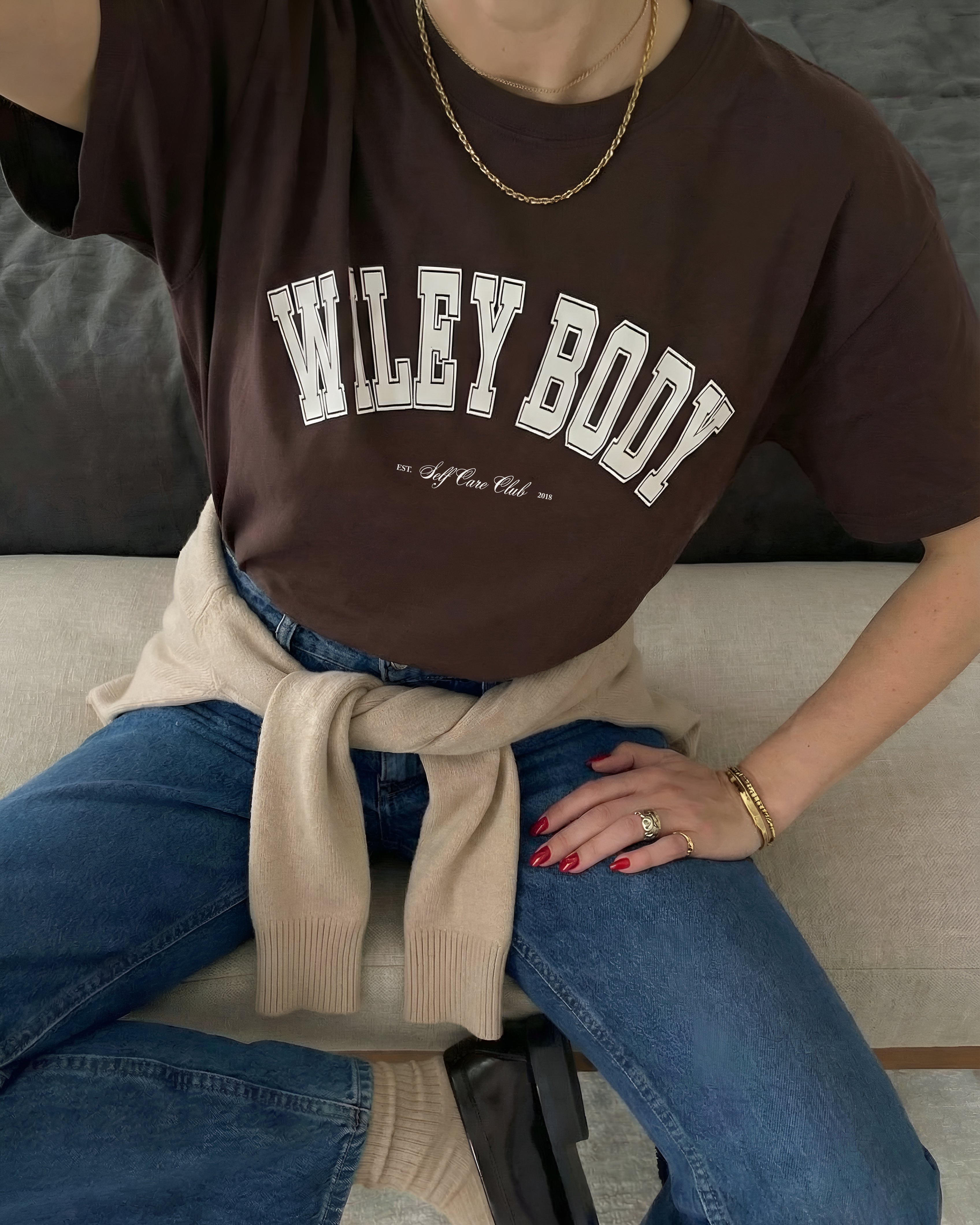 Person wearing a brown 'WILEY BODY' t-shirt sitting on a couch.