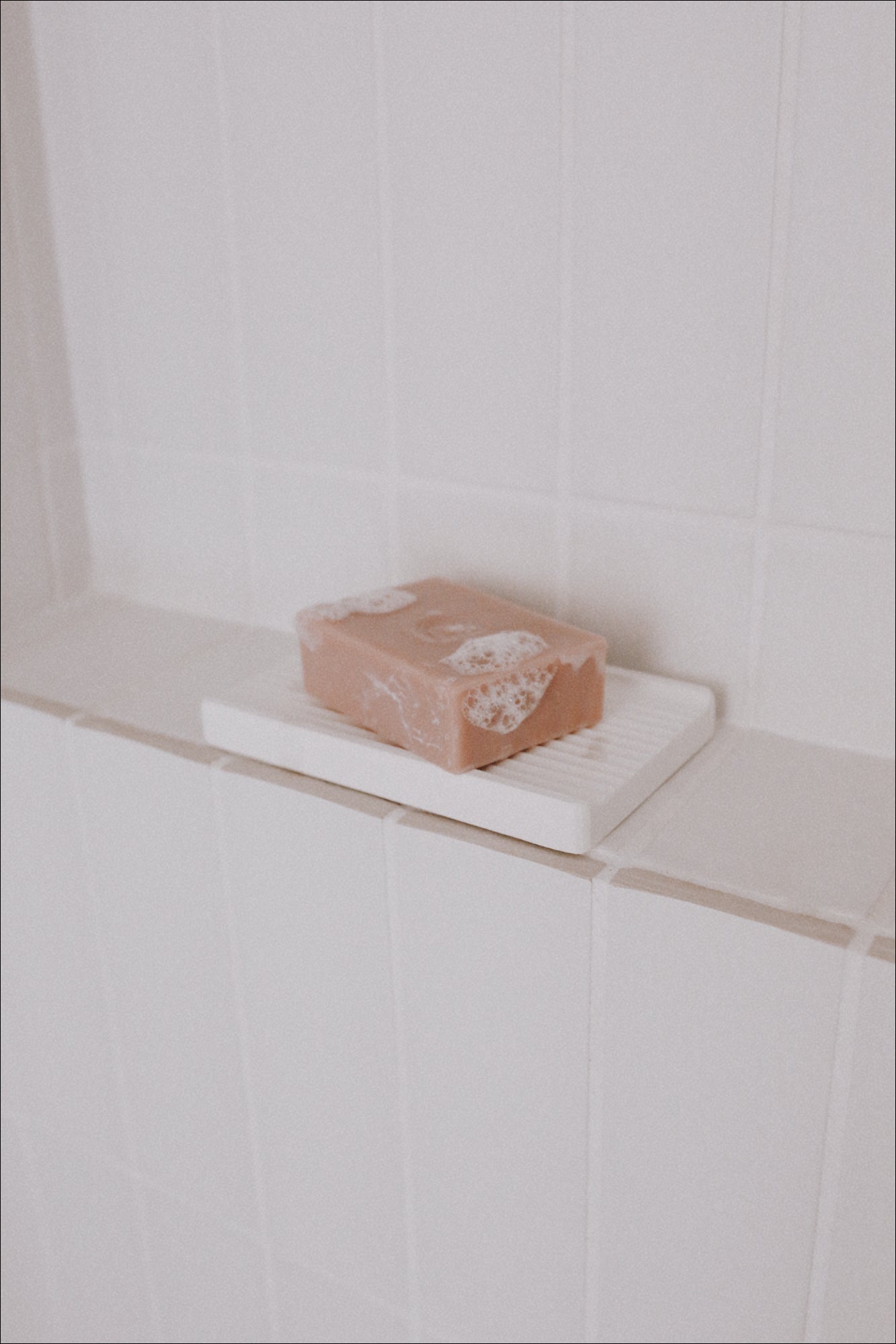 A photo of a Body Bar and Soap Dish on a shelf in a shower with bubbles on the Body Bar
